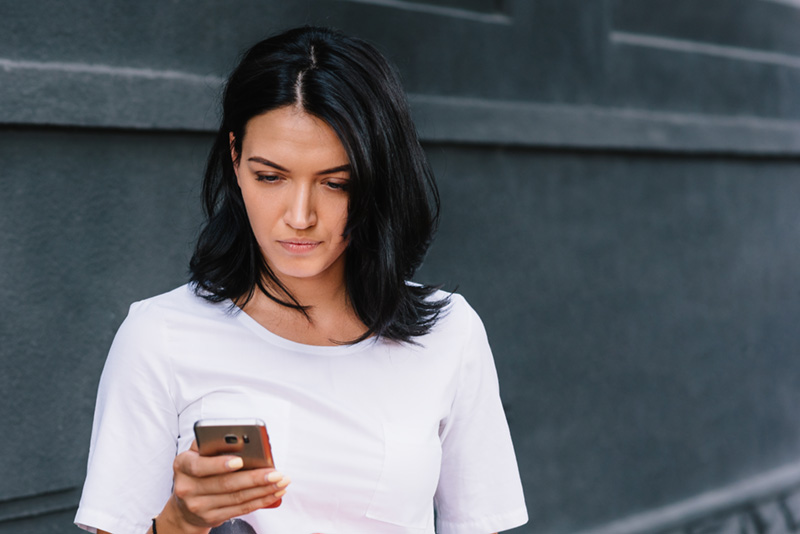 Good looking female in stylish clothes, reads good news on mobil